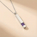 Silver necklace with a rectangular pendant featuring a purple gemstone on a beige background