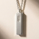 A silver rectangular bar pendant on a chain, featuring three small inset diamonds in the center