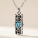 Silver necklace with a cylindrical pendant featuring blue gemstones on a beige background