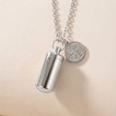 Silver cylindrical pendant on a chain with a round tag against a beige background
