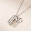 Silver necklace with a cylindrical pendant and paw print charm on a beige background