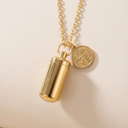 Gold cylindrical pendant with chain on a beige background