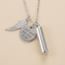 Silver necklace with angel wing charm, round pendant with engraved text, and cylindrical container on beige background