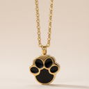 Gold necklace with a black paw print pendant on a beige background