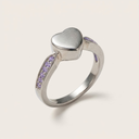 Silver ring with a heart-shaped top and purple gemstones on a light gray background
