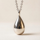 Silver teardrop pendant on a chain against a beige background