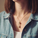Person wearing a gold necklace with a cylindrical pendant, wearing a denim jacket.