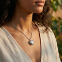 Woman wearing a silver heart-shaped pendant necklace with a blurred natural background