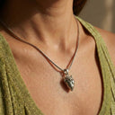 Silver necklace with a heart pendant worn by a person in a green top.