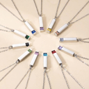 Necklaces with rectangular pendants featuring colored stones arranged in a circular pattern on a beige background.