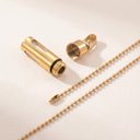 Gold-colored lamp parts including a cylindrical component and a chain on a beige background