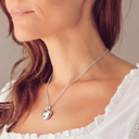 Woman wearing a necklace with a heart pendant against a neutral background