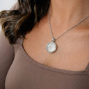 Silver necklace with a round pendant worn by a person in a brown top.