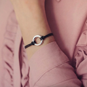 Black bracelet with a silver ring on a wrist, wearing a pink shirt.