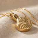 Gold scallop shell necklace on a beige fabric background