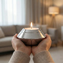 Candle holder with a lit candle held by hands in a cozy living room.