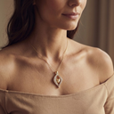 Woman wearing a gold necklace with a pendant against a neutral background