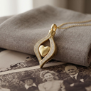 Gold heart-shaped pendant on a chain, resting on vintage photos and fabric.