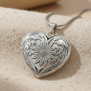 Silver heart-shaped locket with floral design on a beige fabric background