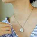 Person wearing a silver necklace with a round pendant, blurred background
