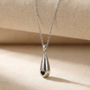 Silver teardrop-shaped pendant necklace on a beige fabric background