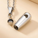 Metallic pendant on a chain next to a cylindrical metal container on a beige background