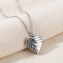 Silver heart-shaped pendant necklace with engraved text on a beige fabric background