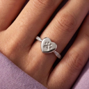 Silver heart-shaped ring with paw print on a person's finger against a pink fabric background