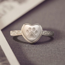Silver heart-shaped ring with paw print design on a textured surface