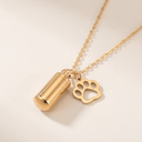 Gold necklace with a cylindrical pendant and paw-shaped charm on a light beige background