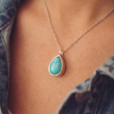 Turquoise teardrop pendant necklace on a person wearing a denim shirt.