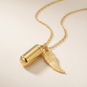 Gold necklace with a cylindrical pendant and angel wing charm on a beige background
