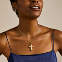 Woman wearing a gold cross necklace against a neutral background