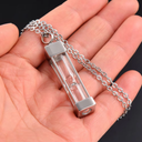 Glass hourglass pendant on a chain held in a hand against a black background