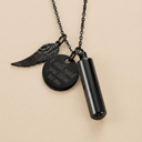 Black pendant necklace with wing charm and engraved message on a beige background