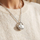 Silver necklace with a pendant on a person wearing a beige sweater