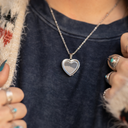 Heart-shaped locket on a chain worn by a person with a dark blue shirt.