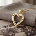 A gold-and-white heart-shaped locket resting on a textured grey cloth, positioned above a vintage black-and-white photograph of a family.