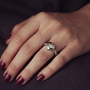 Hand wearing a silver ring with a heart-shaped center on a dark background