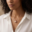 Woman wearing a gold necklace with a heart pendant against a neutral background