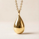Gold teardrop pendant necklace on a beige background