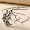 Silver fish-shaped pendant on a chain against a beige background